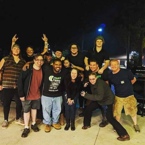 A diverse group of people poses together outdoors at night, smiling and making playful gestures.