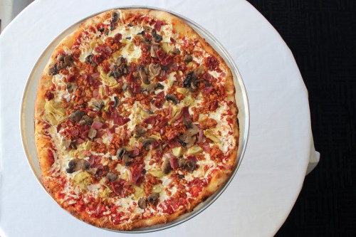 A large pizza topped with cheese, pepperoni, mushrooms, onions, and artichokes on a round silver platter.