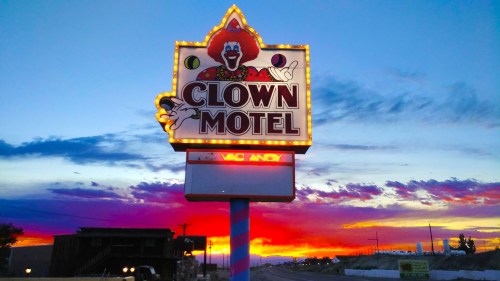 A colorful motel sign featuring a clown, illuminated against a vibrant sunset sky.