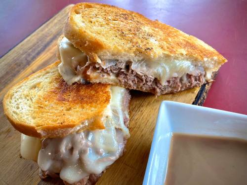 A toasted sandwich filled with melted cheese and shredded meat, served with a small dish of dipping sauce.