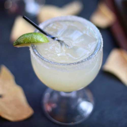 A refreshing margarita in a glass with a salted rim, garnished with a lime wedge, surrounded by tortilla chips.