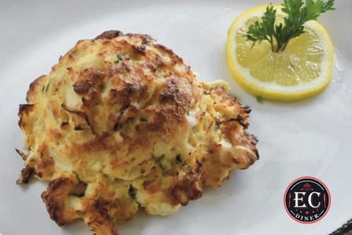 A golden-brown crab cake served with a lemon wedge and parsley on a white plate.