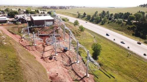 Aerial view of a construction site with roller coaster supports near a highway and a small town in the background.