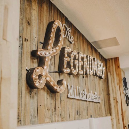 Sign reading "The Legendary Milkshake Bar" with illuminated letters on a wooden wall.