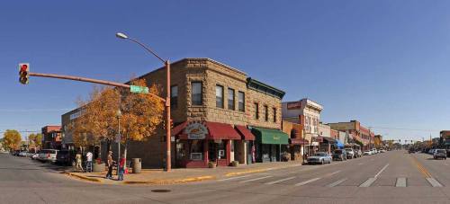 A sunny street scene featuring historic buildings, shops, and autumn trees in a small town.