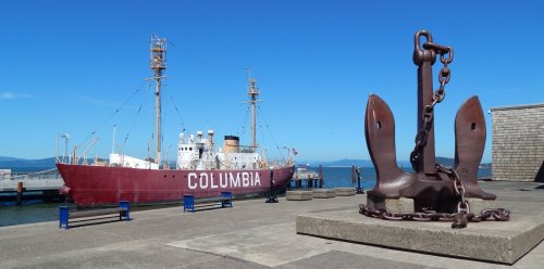 A historic ship named "Columbia" docked beside a large anchor on a sunny day by the water.