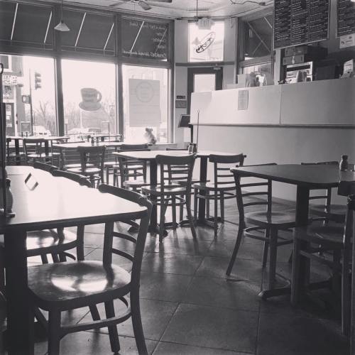 A cozy café interior with empty tables and chairs, large windows letting in natural light.