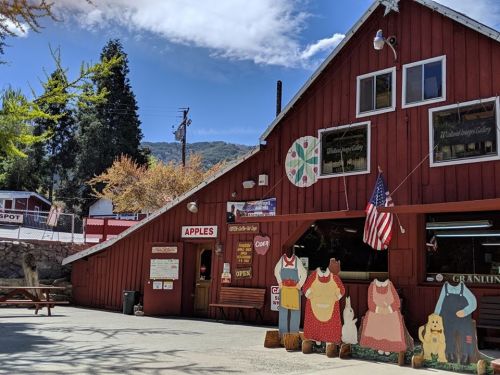 Red barn-style building with an "Apples" sign, picnic tables, and colorful cutouts of dresses and animals outside.