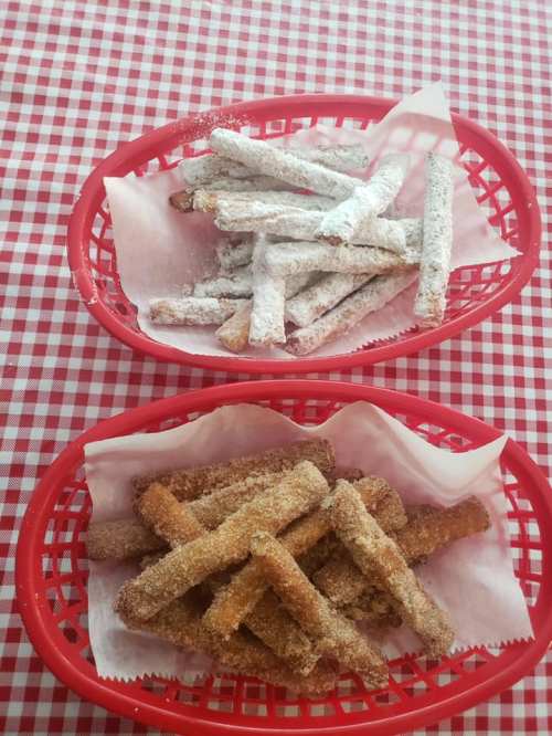 Two red baskets on a checkered tablecloth, one filled with powdered sugar-coated treats and the other with cinnamon-sugar treats.