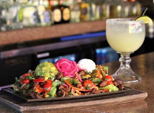 A vibrant plate of nachos topped with guacamole, tomatoes, and pickled onions, alongside a margarita in a glass.