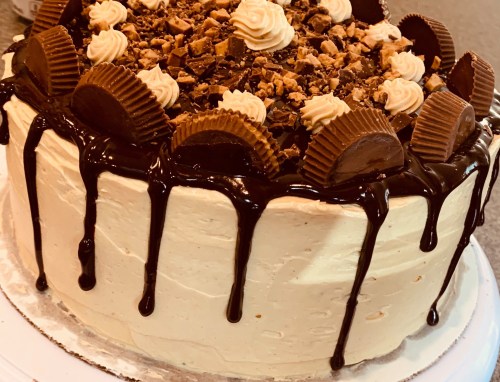 A decadent chocolate cake topped with crushed candies, chocolate drizzle, and peanut butter cups.