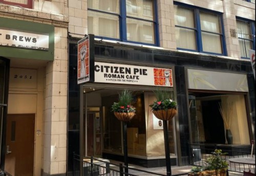 Exterior of Citizen Pie Roman Cafe, featuring a sign and decorative planters, in an urban setting.