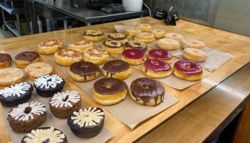 A variety of colorful donuts displayed on a wooden table, including glazed, chocolate, and decorated options.