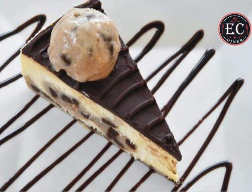 A slice of chocolate chip cheesecake topped with a scoop of cookie dough ice cream, drizzled with chocolate sauce.