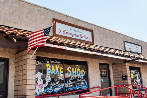A bakery storefront with a sign reading "Chef Flemming's European Bakery" and an American flag. Colorful window displays.