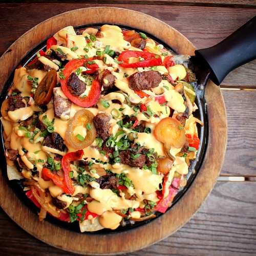 A sizzling platter of nachos topped with beef, jalapeños, bell peppers, and drizzled with cheese sauce and green onions.