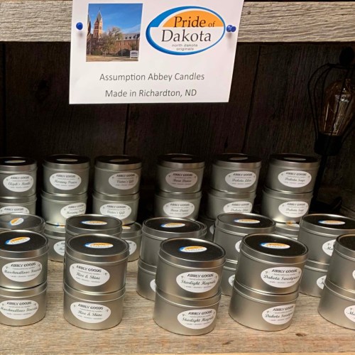 A display of Assumption Abbey Candles in metal tins, labeled and organized on a wooden shelf.