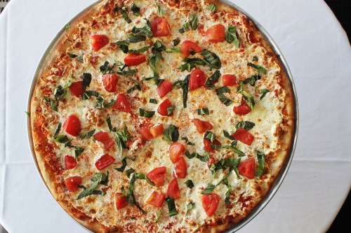 A large pizza topped with fresh tomatoes and basil on a white tablecloth.
