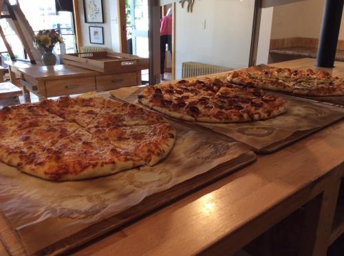 Three large pizzas on wooden trays, showcasing various toppings, placed on a table in a cozy restaurant setting.