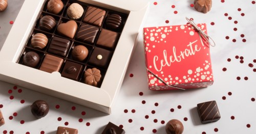 A box of assorted chocolates next to a red gift box with "Celebrate!" written on it, surrounded by scattered confetti.