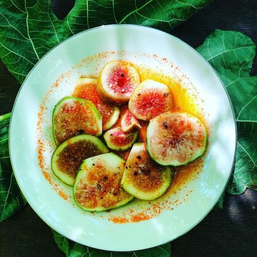 A white plate with sliced figs sprinkled with spices, surrounded by large green leaves.