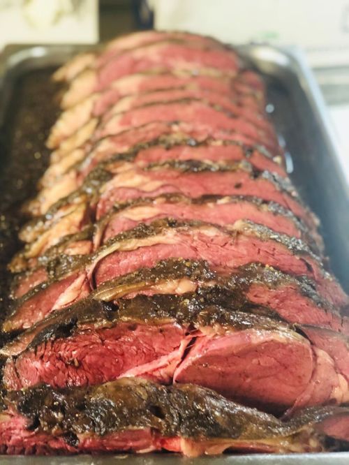 Sliced roast beef arranged neatly on a tray, showcasing a rich, dark crust and juicy pink interior.