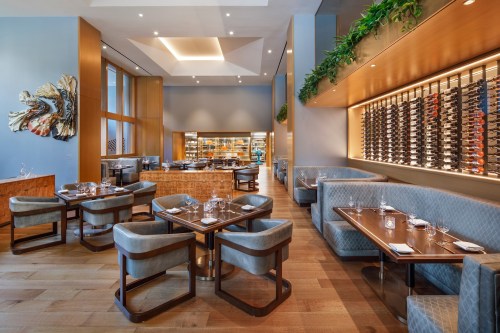Modern restaurant interior featuring elegant seating, wooden tables, and a wine display against a stylish backdrop.