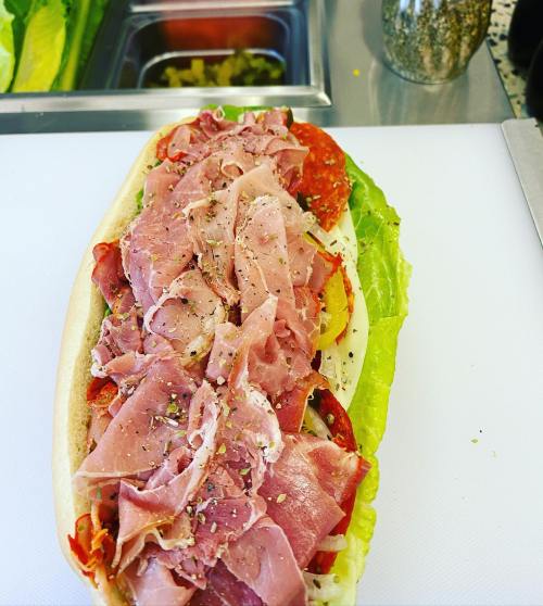 A sub sandwich loaded with layers of deli meats, lettuce, and spices on a white cutting board.