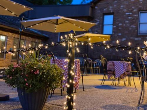 Outdoor dining area with string lights, checkered tablecloths, and potted flowers, set in a cozy evening atmosphere.