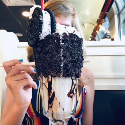 A tall dessert glass filled with chocolate ice cream, topped with whipped cream, an Oreo cookie, and a straw.
