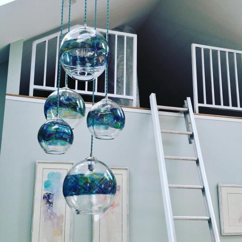 Hanging glass orbs with colorful patterns, a ladder nearby, and a loft area in a modern interior space.