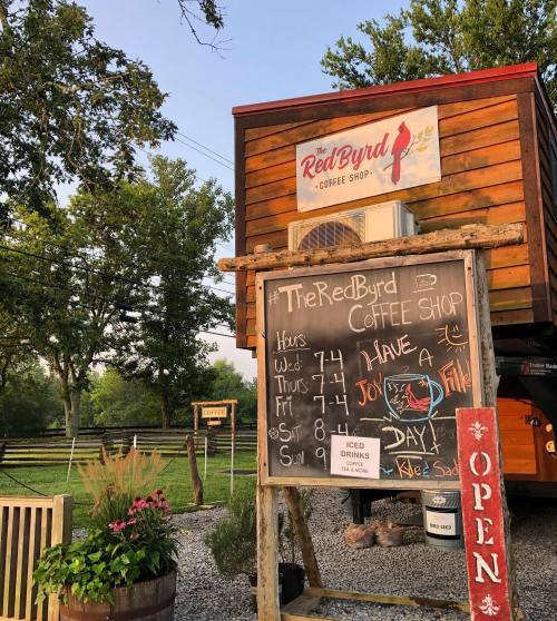 A cozy coffee shop with a wooden exterior, featuring a sign and a chalkboard displaying hours and menu items.