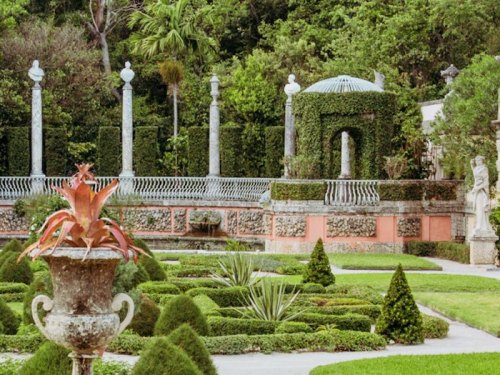 Lush garden with manicured hedges, stone columns, and a decorative urn in a serene, green landscape.