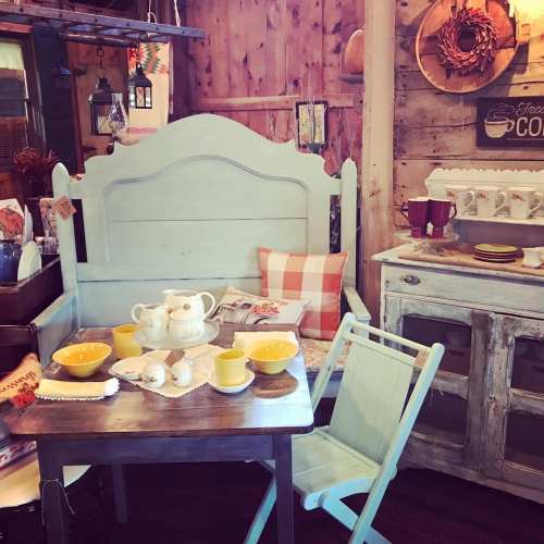 A cozy vintage-inspired corner with a light blue bench, wooden table, yellow dishes, and rustic decor.