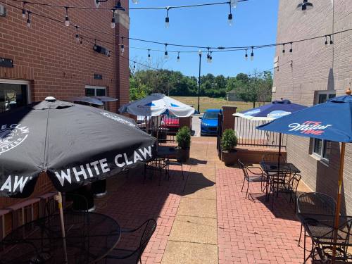 Outdoor patio with tables and umbrellas, string lights overhead, and a view of parked cars and greenery in the background.