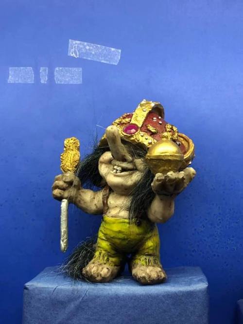 A whimsical troll figure with a colorful hat, holding a golden orb and a staff, set against a blue background.
