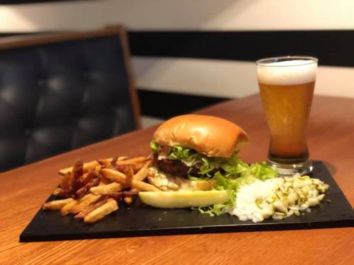 A delicious burger with lettuce, served with fries, pickles, and a glass of beer on a wooden table.