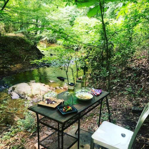 A small table by a stream in a lush green forest, adorned with jars and a plate of snacks.