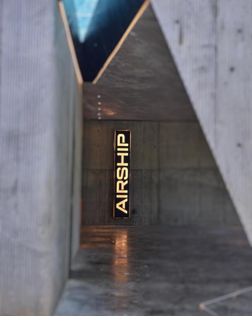 A modern interior with a concrete wall featuring a vertical sign that reads "AIRSHIP." Soft lighting enhances the space.