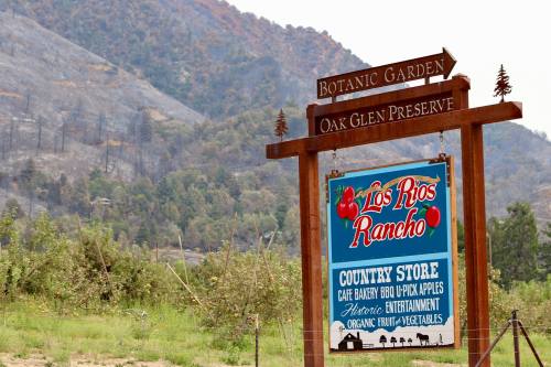 Sign for Los Rios Rancho, featuring a country store, café, and botanic garden, with a backdrop of charred hills.