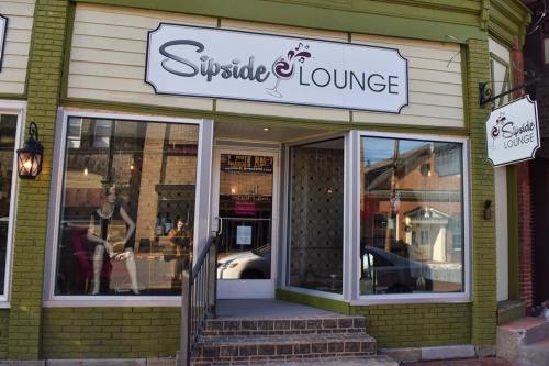 Exterior of Sipside Lounge, featuring a green brick facade, large windows, and a sign with a cocktail logo.