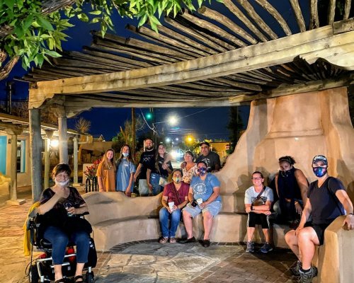 A group of people wearing masks gathers under a wooden structure at night, smiling and posing for the photo.
