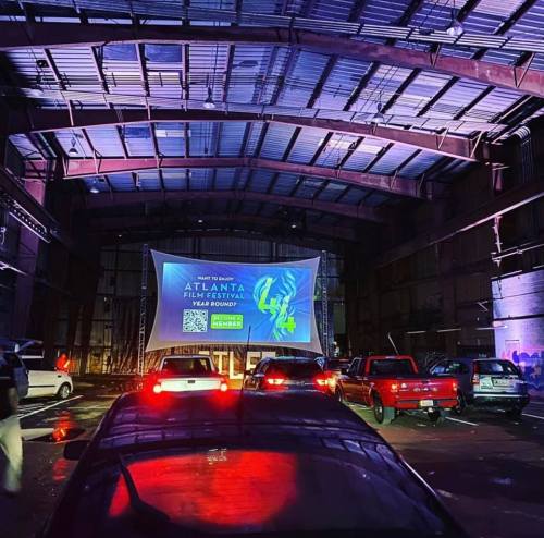 Cars parked inside a warehouse, facing a large screen displaying the Atlanta Film Festival logo and event details.