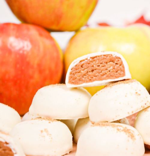 A stack of white chocolate-covered treats with a cinnamon filling, surrounded by fresh red and green apples.