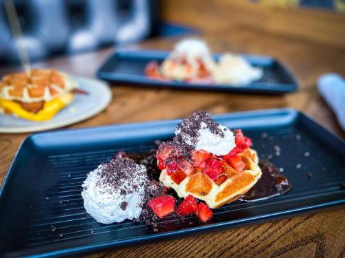 A plate of waffles topped with strawberries, whipped cream, and chocolate sauce, served on a black rectangular dish.