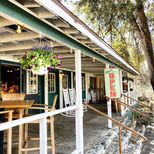 A charming storefront with a sign reading "OPEN," featuring hanging plants and a welcoming porch with rocking chairs.