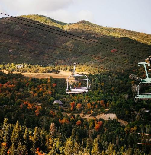A ski lift chair suspended over a colorful autumn landscape with mountains and trees.
