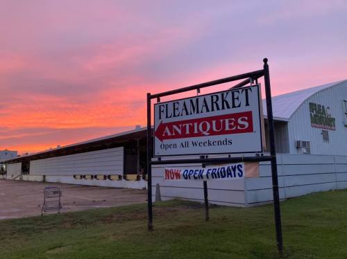 Sign for a flea market and antiques store at sunset, with "Open All Weekends" and "Now Open Fridays" displayed.