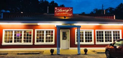 A cozy café named Clancy's, featuring a red exterior and large windows, illuminated at dusk.
