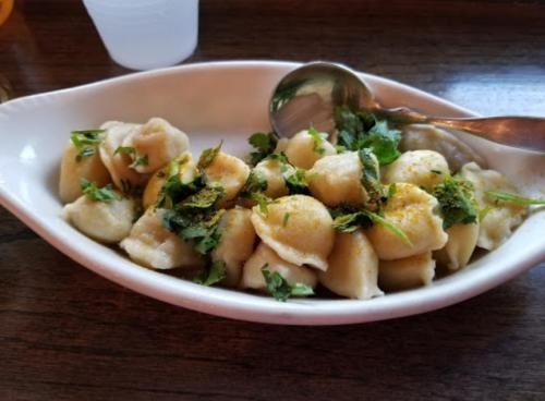 A white dish filled with dumplings topped with fresh herbs and a sprinkle of seasoning.